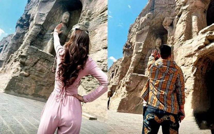 游客在云冈石窟拍摄与大佛击掌留念照。