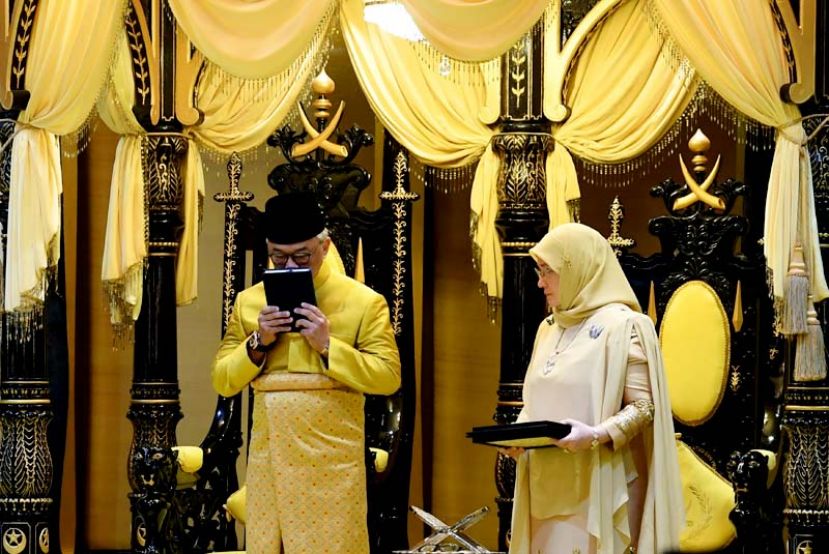 图:苏丹阿都拉在宣誓就任彭亨第六任苏丹的仪式上亲吻可兰经。右为苏丹后东姑阿兹莎。